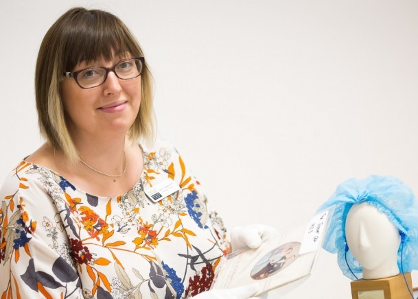 A woman sitting at a table wearing whitle gloves and holding a photograph of a couple in a white mount.