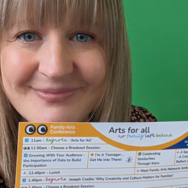 A smiling woman holds a piece of paper with the title 'family arts conference' at the top