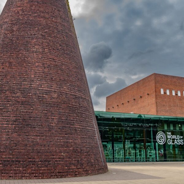 A large brick tower next to a glass building. Signage on the building reads 'The World of Glass'