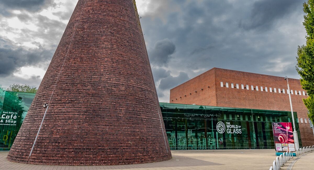 A large brick tower next to a glass building. Signage on the building reads 'The World of Glass'