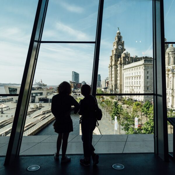 Two people in front of a large glass window overlooking Liverpool waterfront