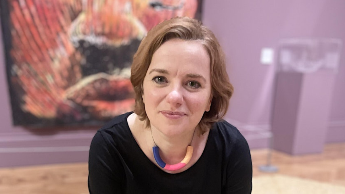 A woman smiling. There is an artwork in the background.